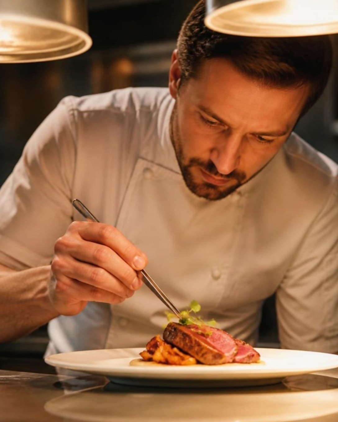 Chef garnishing a plated dish at the kitchen pass