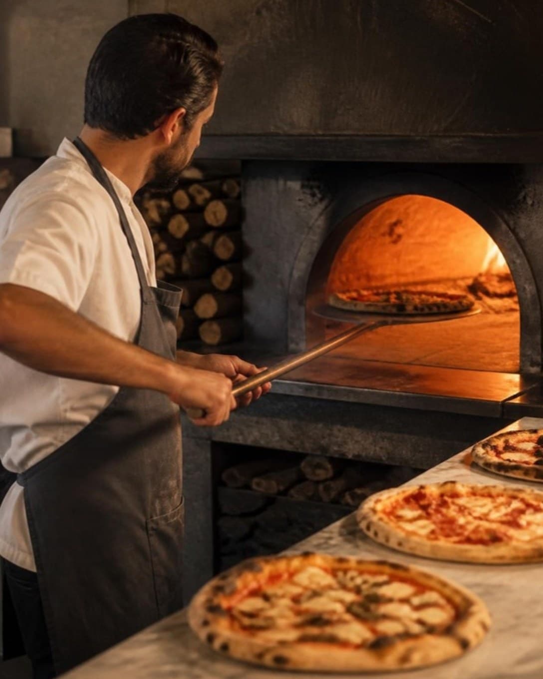 Pizza chef sliding a pizza into a wood-fired oven