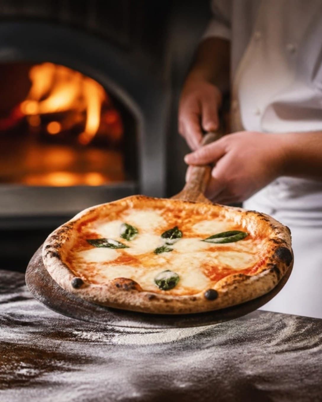 Wood-fired pizza lifted from the oven on a wooden peel